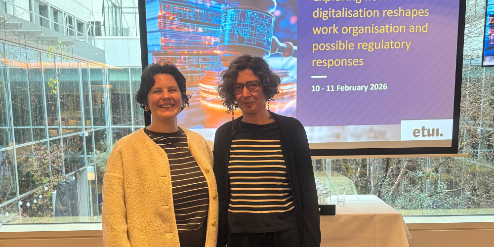 Michela Trentin and Dora Fonseca standing in front of a presentation screen showing the ETUI Future of Work conference title 'Exploring how digitalisation reshapes work organisation and possible regulatory responses'