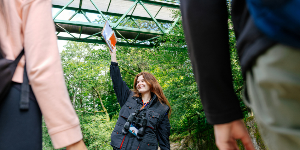 A tour guide with one arm raised holding a clipboard and map